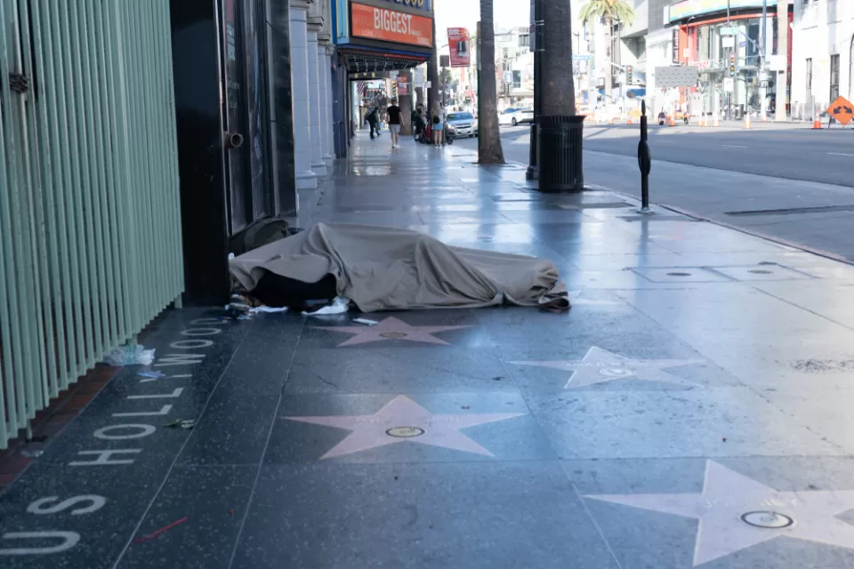A person experiencing homelessness sleeps on the sidewalk, atop the stars on the Hollywood Walk of Fame.
